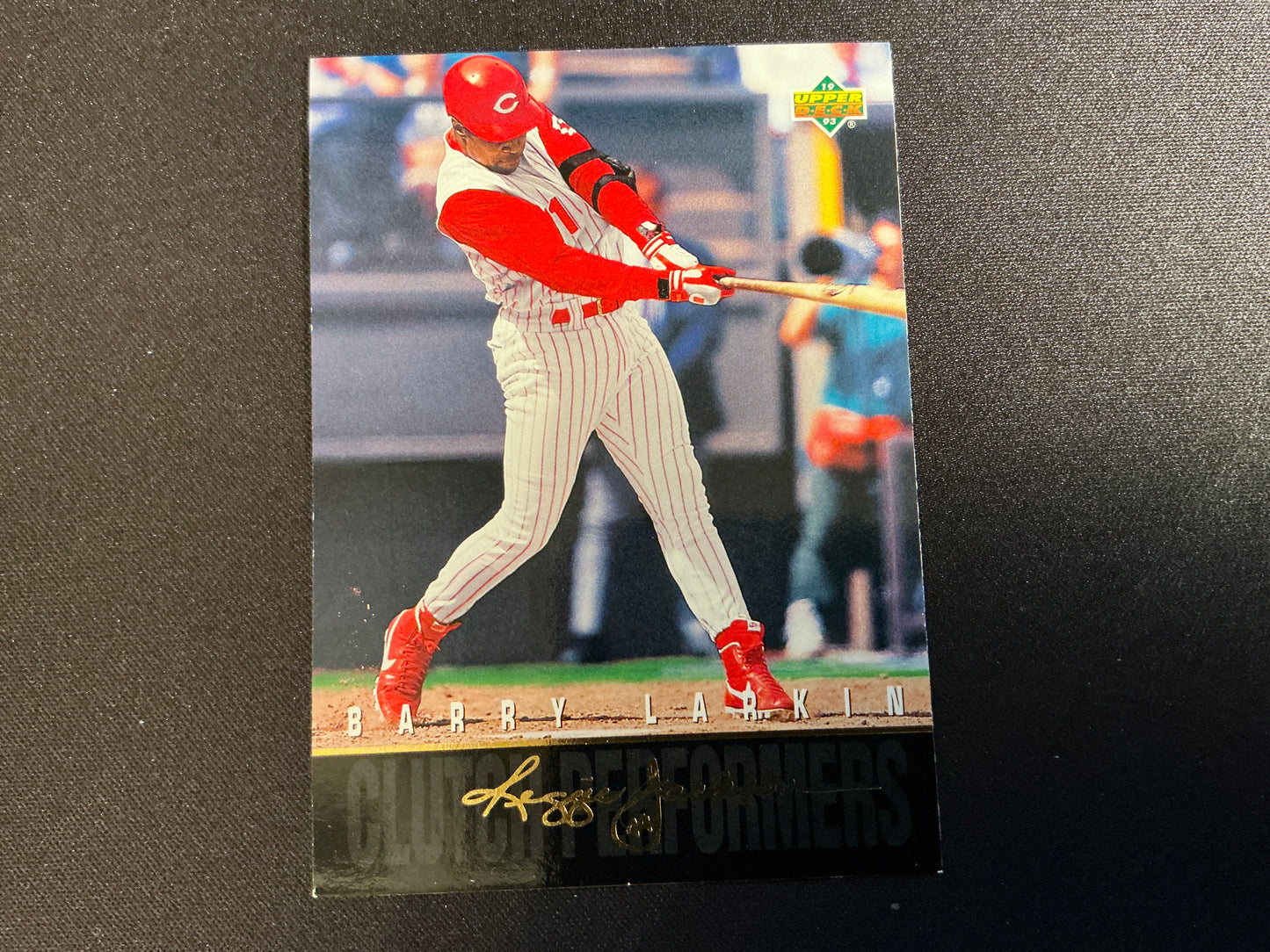 A 1993 Upper Deck Clutch Performers baseball card featuring Reds player Barry Larkin in mid-swing with a red and white striped uniform, signed by Larkin.